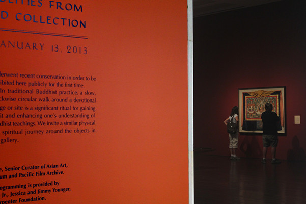 Two visitors are watching one of the thangkas on the wall.